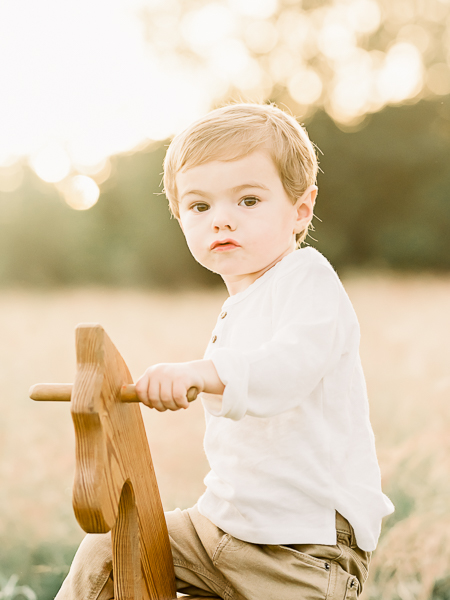 Little toddler boy sitting on wood rocking horse during photography session in Katy area field