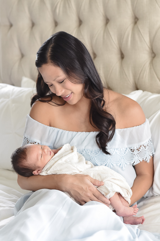 mom on bed holding newborn baby during in home newborn photography session.