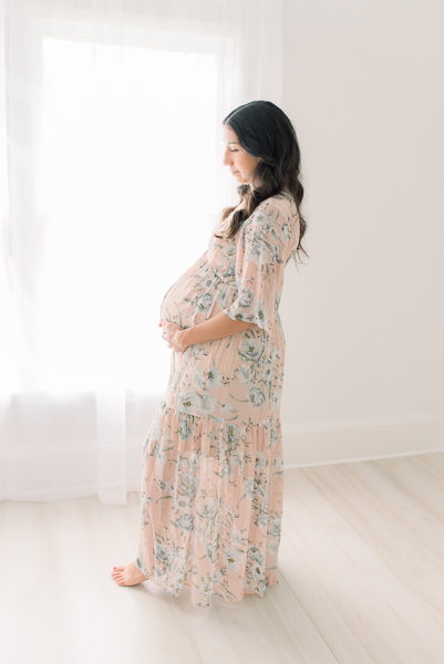 Expectant mom in pink dress during Houston Height maternity session with mom standing in front of window