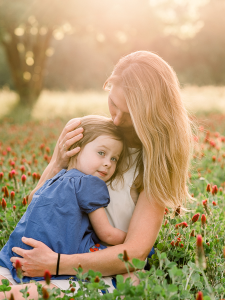 Mom holding daughter with toddler snuggling in on mom during sunset in Houston wildflower field during photography session.