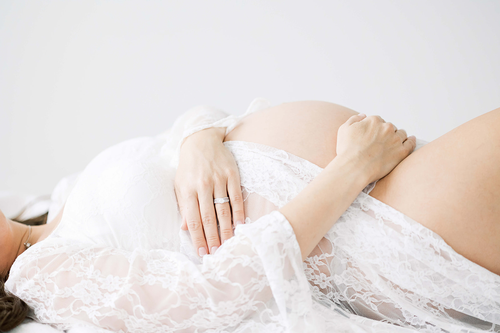 A mother to be lays on a bed in a sheer lace maternity gown before her 3D Ultrasound Houston