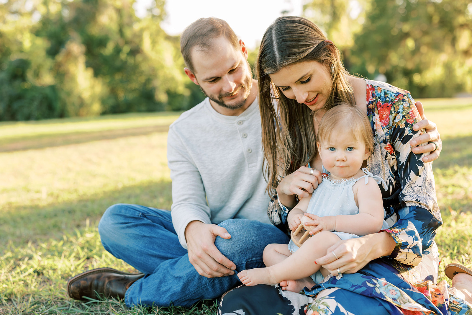 Happy mom and dad sit in a park at sunset playing with wooden toys with their infant daughter in mom's lap