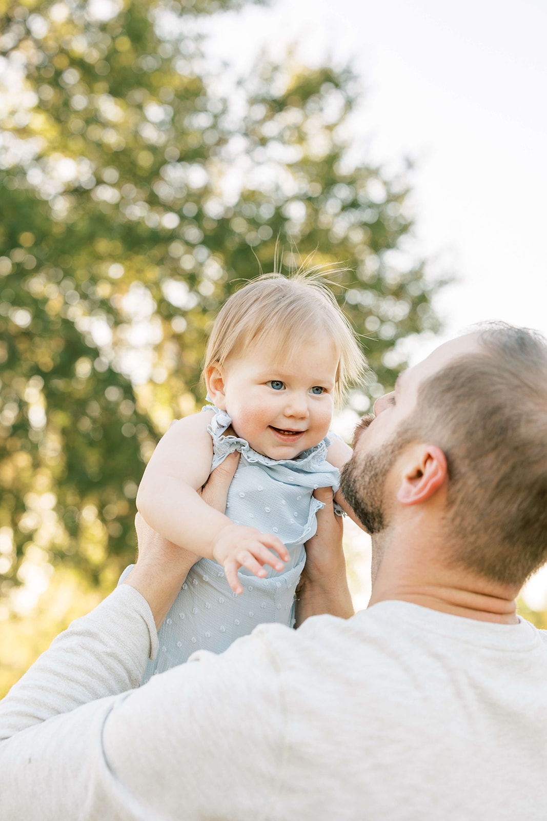 A happy infant is lifted and kissed by dad in a park at sunset after some Baby Music Classes Houston