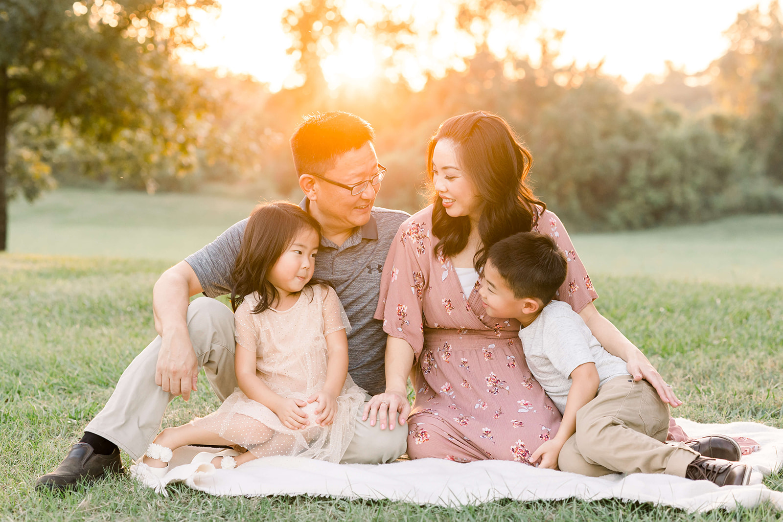 Happy parents smile at each other while sitting and playing on a picnic blanket in a park at sunset with their toddler son and daughter after visiting Dentini Pediatric Dentistry