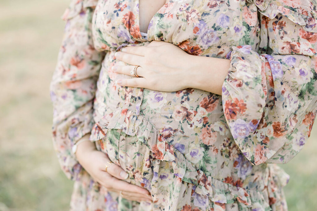 Details of a mother to be in a floral print dress holding her bump