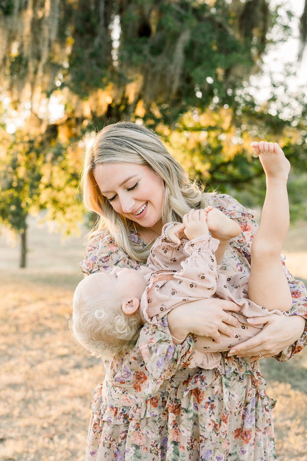 A happy mother plays with her toddler daughter in her arms in a park at sunset after using a Houston Birthing Center