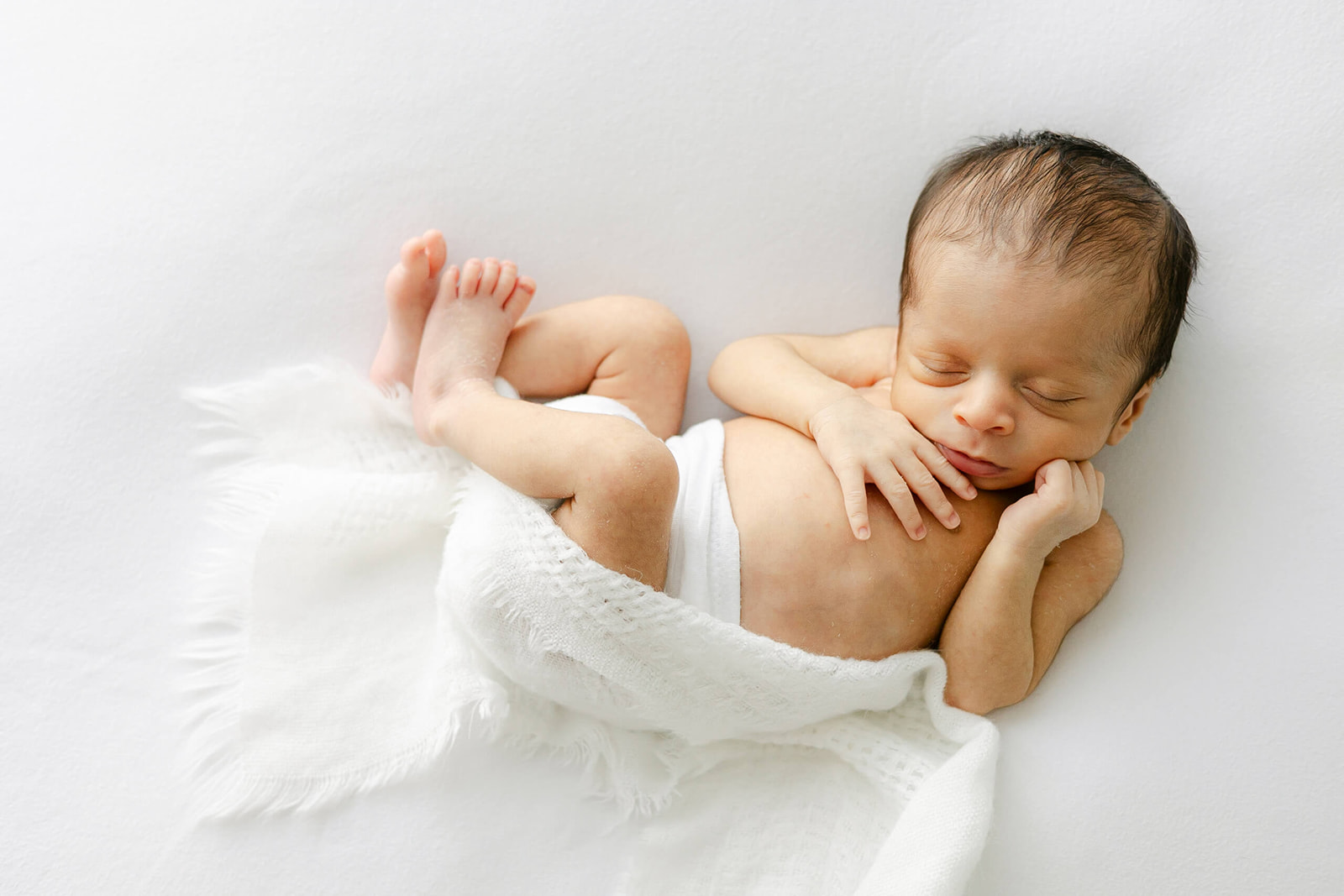 A newborn baby lays wrapped loosely in a white blanket in a studio sleeping thanks to Houston lactation consultants