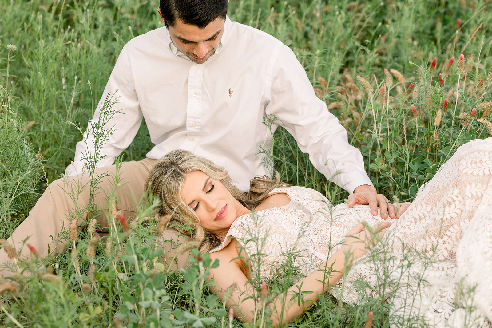 A mom to be lays in a field of wildflowers while resting her head in her husbands lap after visiting with Houston Midwives