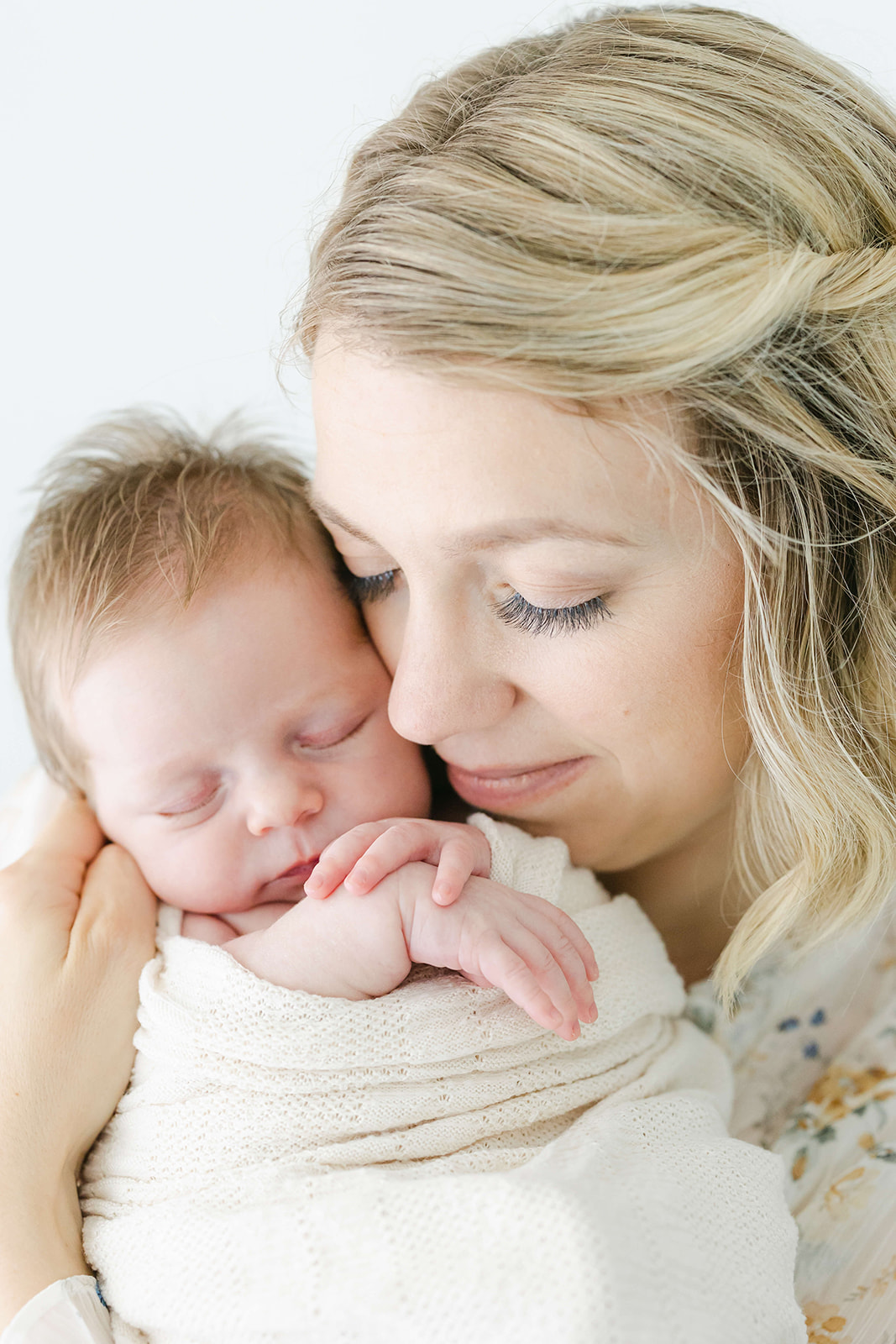 A happy mom snuggles her sleeping newborn baby in a studio