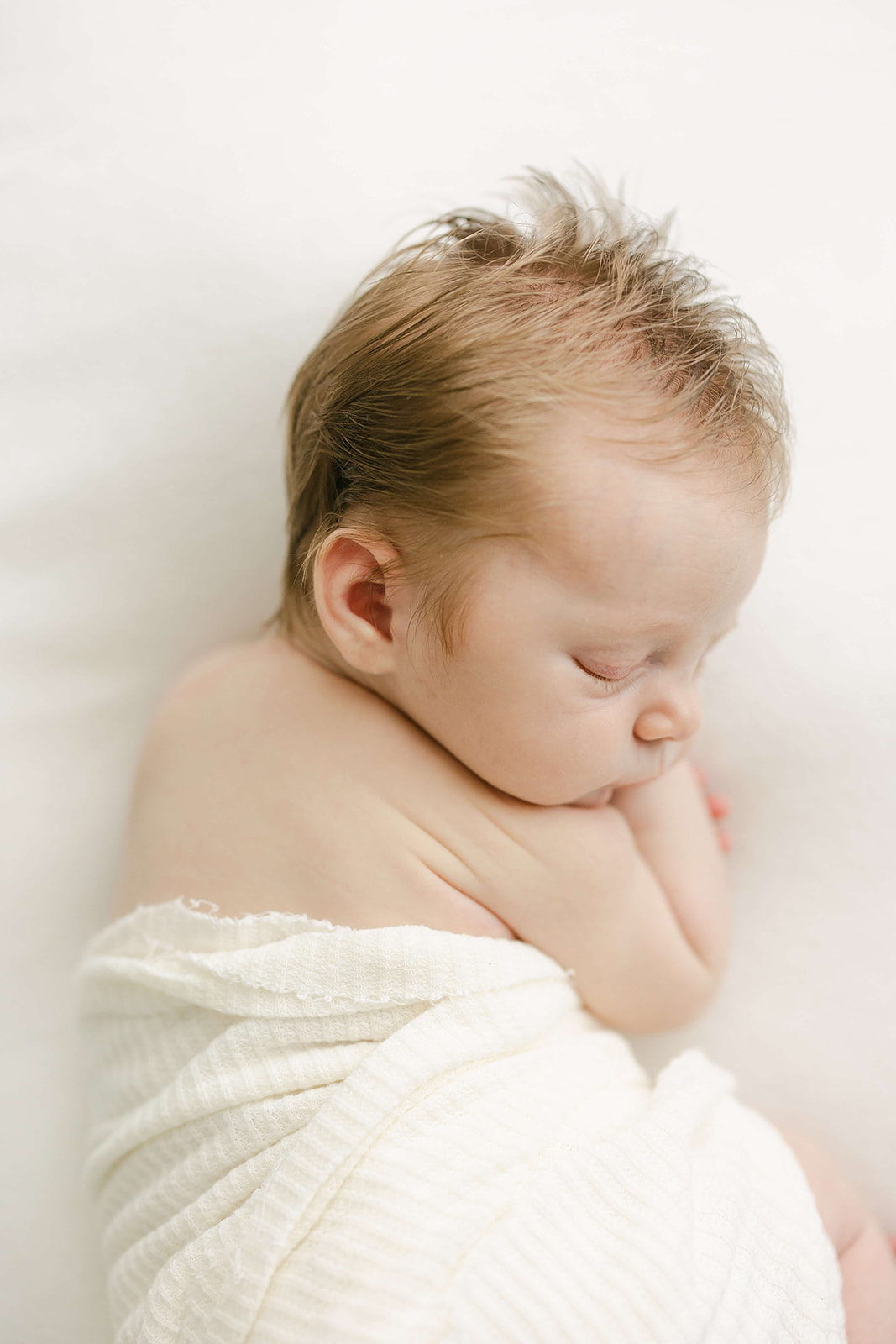 A newborn baby sleeps in a white half swaddle in a studio