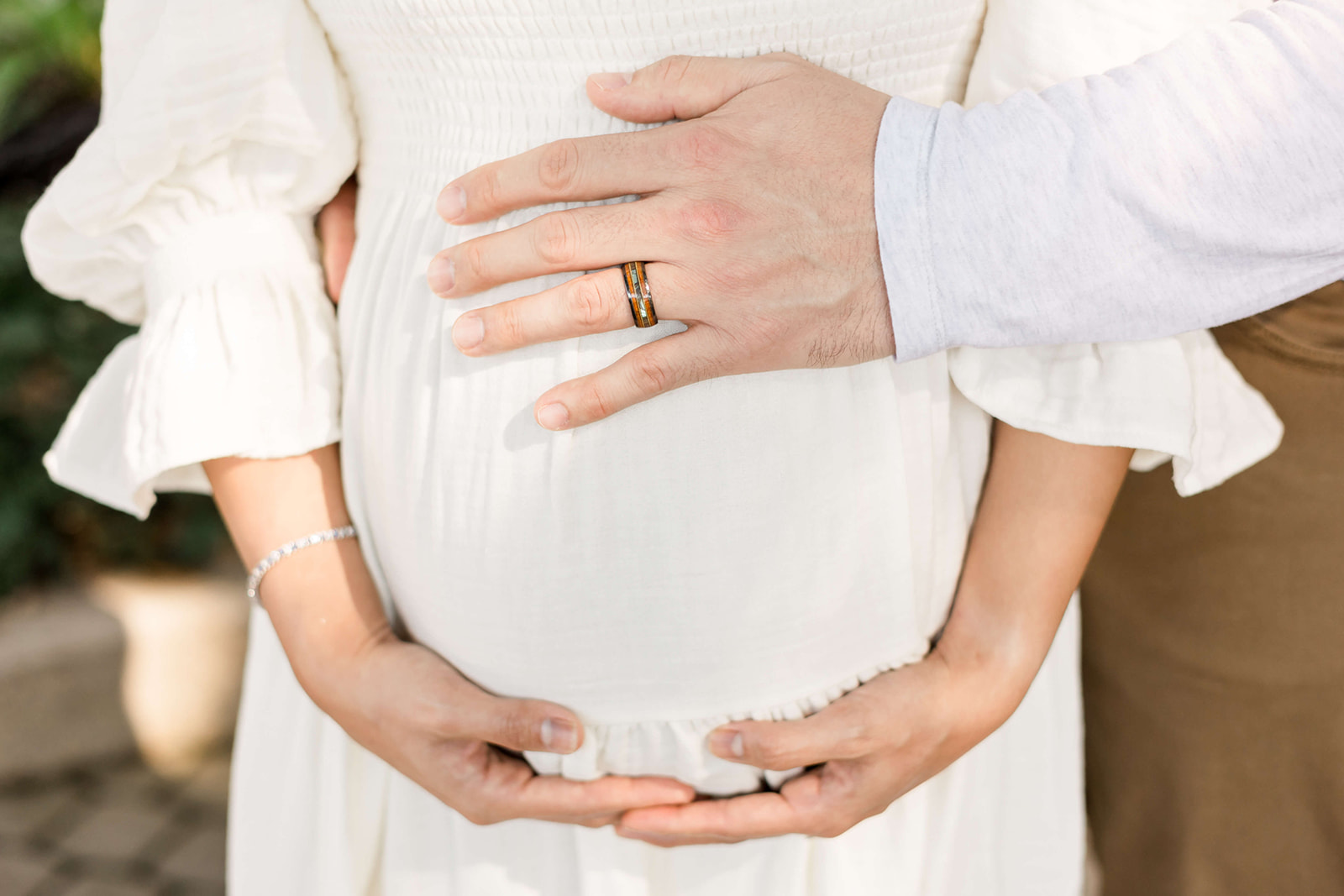 Details of expecting parents holding the bump in a white maternity dress after visiting North Houston Birth Center