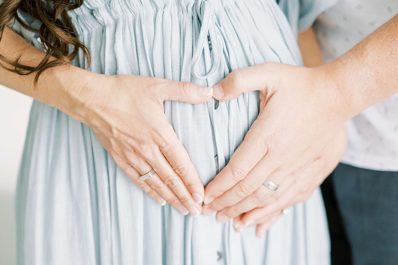 Details of expecting parents making a heart with their hands on the bump in a blue dress