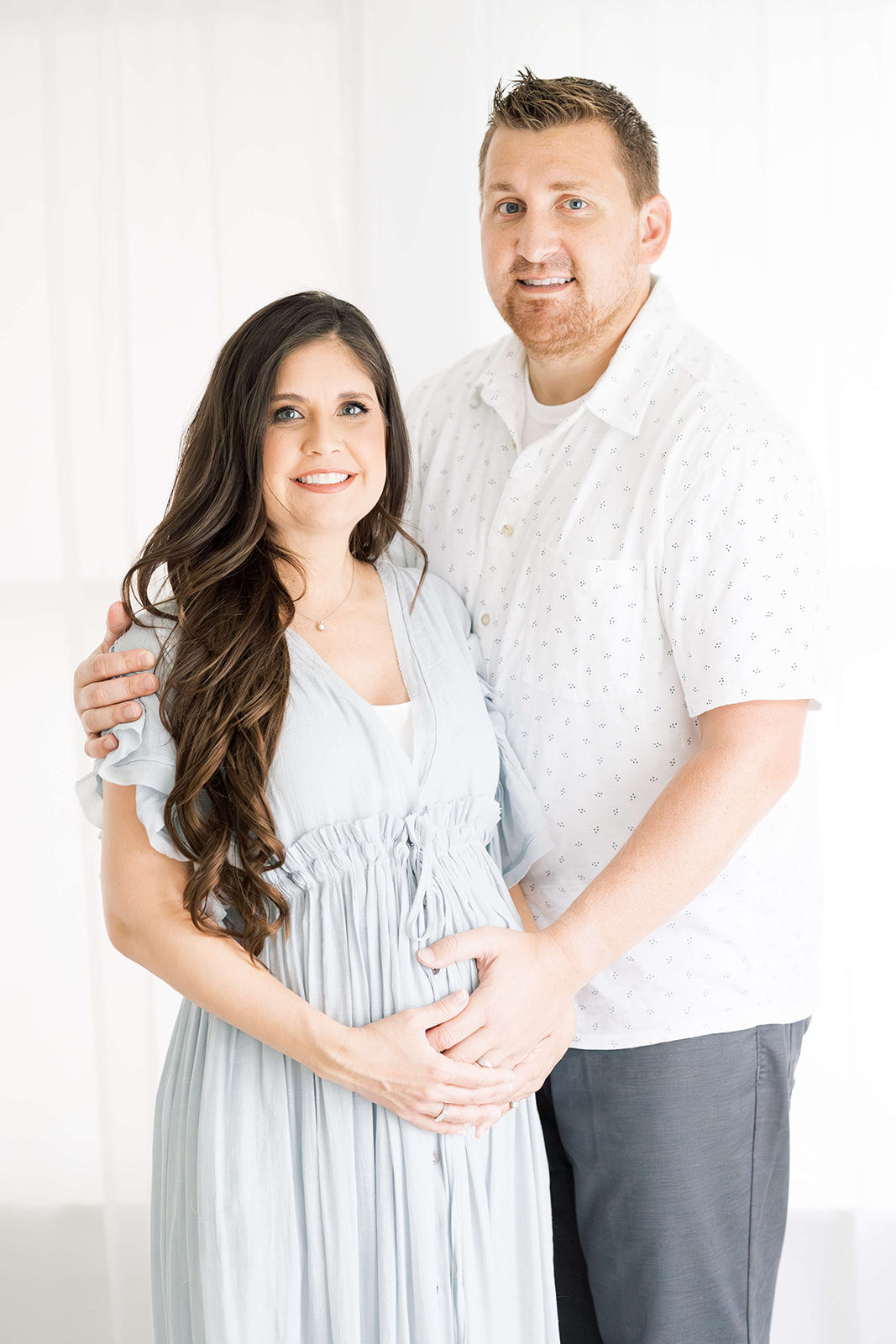 Happy expecting parents stand in a studio holding the bump after visiting with Premier Doulas of Houston