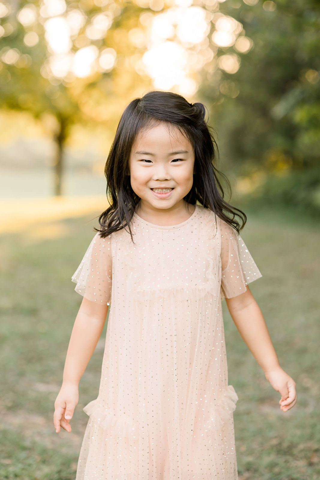 A toddler girl in a pink sparkly dress smiles while exploring a park at sunset after visiting Sweet Bambini