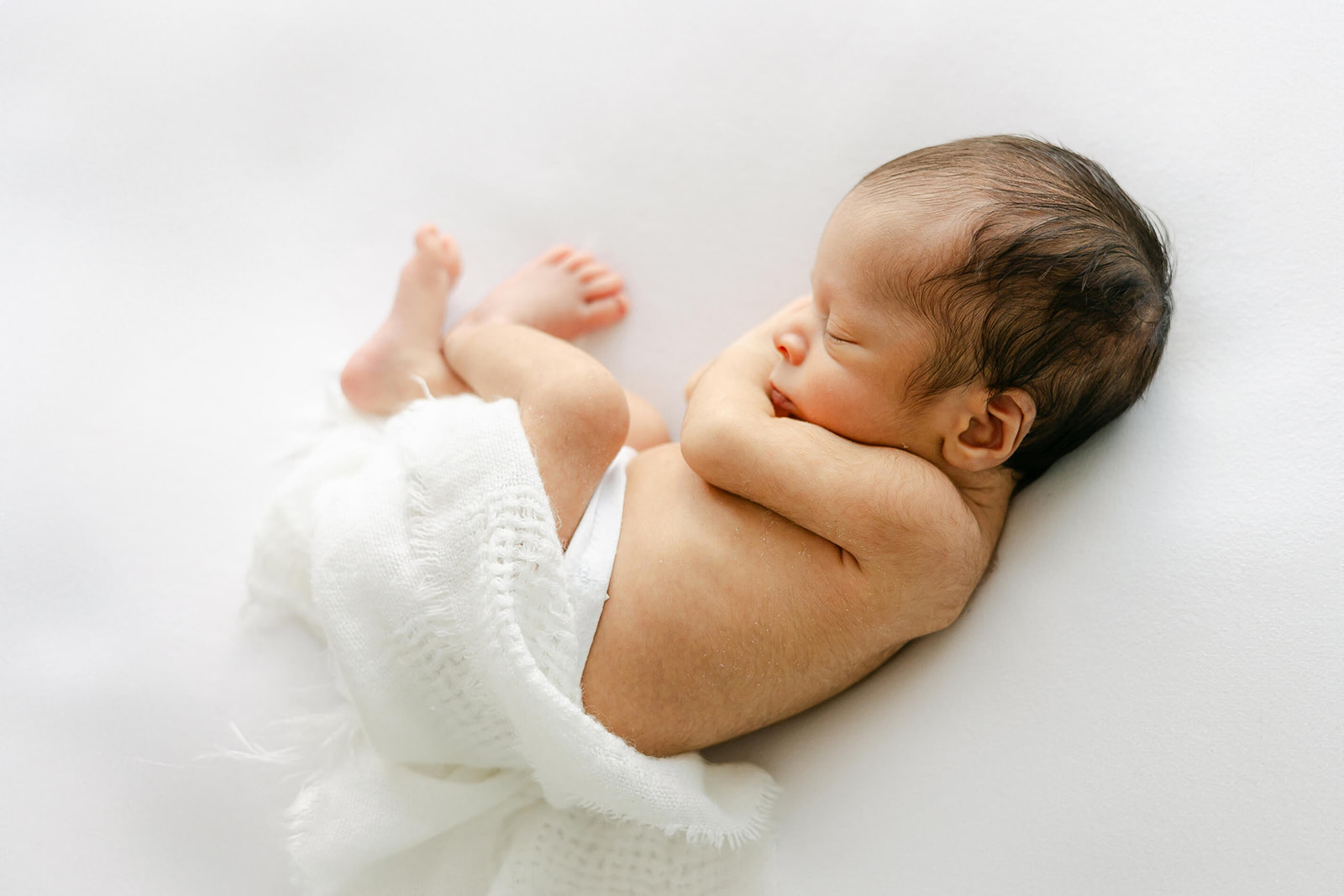 A newborn baby sleeps while wrapped in a white blanket on a white bed in a studio after meeting Texas Lactation Consultants