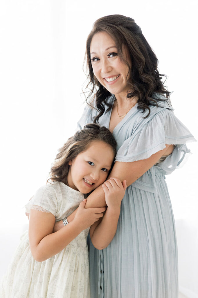 A mother in a blue dress hugs her daughter while standing in a studio after visiting Threadfare
