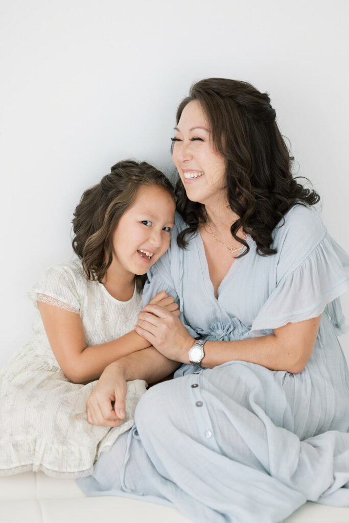 A mother and daughter laugh and cuddle while playing on a bed in a studio