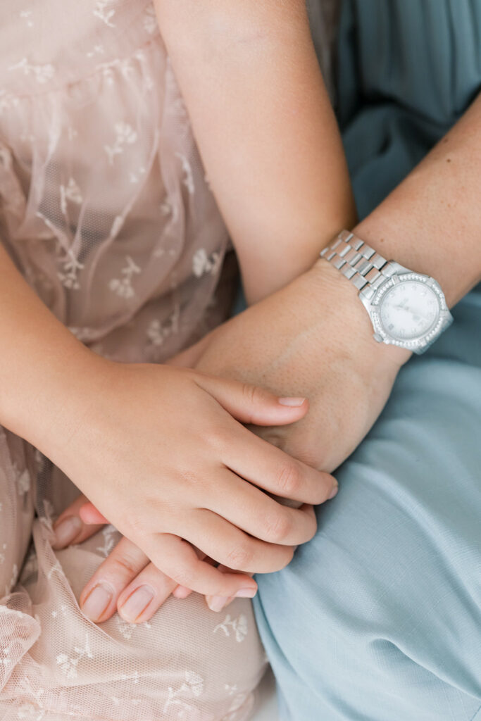 Details of a mom and daughter sitting together holding hands in mom's lap