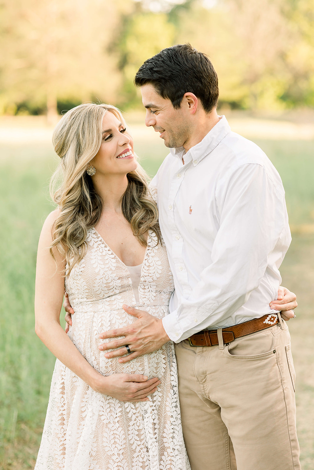 Happy expecting parents stand in a field hugging with hands on the bump after meeting Concierge Doulas of Houston