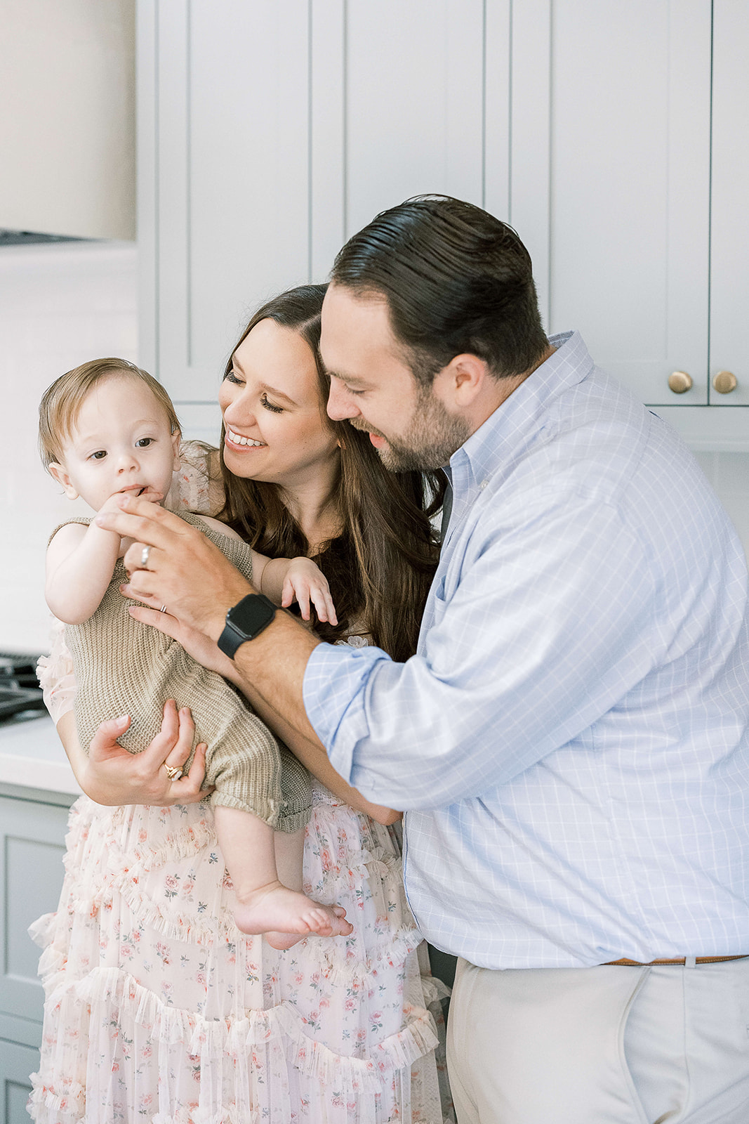 Happy parents play with their toddler son sitting on mom's hip in a kitchen after visiting Houston Baby Boutiques