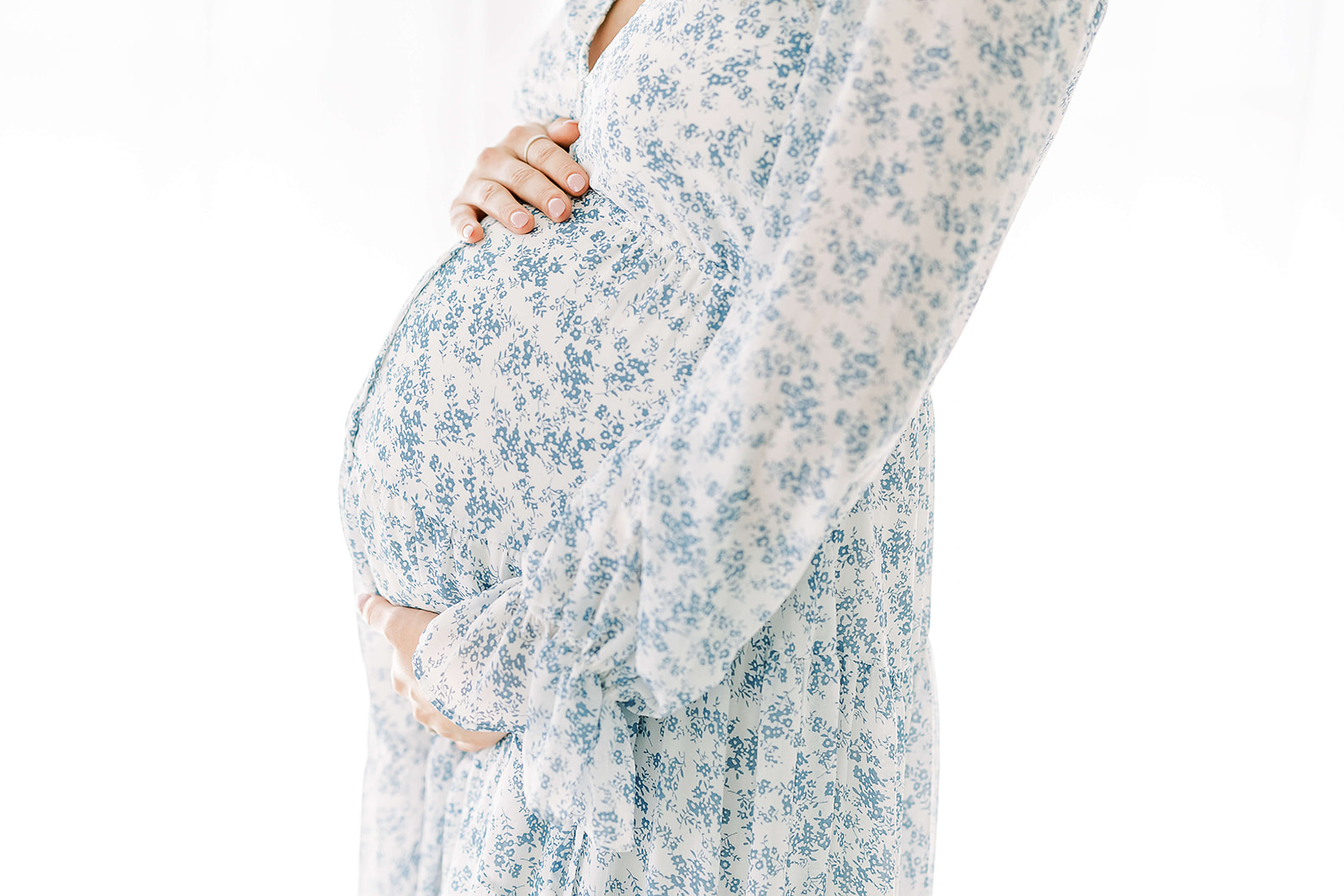 A profile view of a mother to be in a blue floral print maternity gown holding her bump before visiting her Houston OBGYN