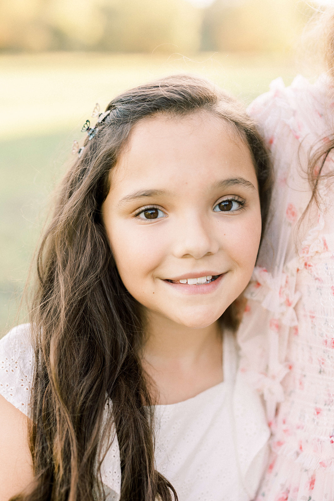 A young girl with dark hair and a white dress stands with mom in a park before visiting Houston pediatric dentists