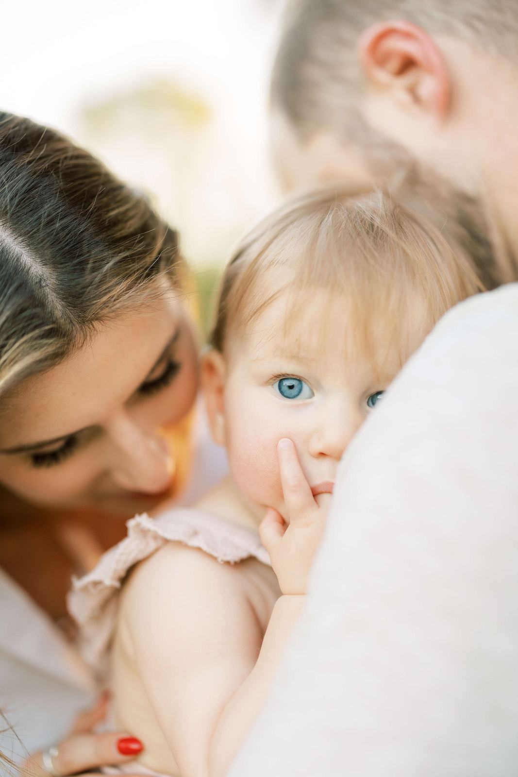 A toddler girl sucks on a finger while snuggling with mom and dad in a park at sunset before visiting Children's Boutiques in Houston