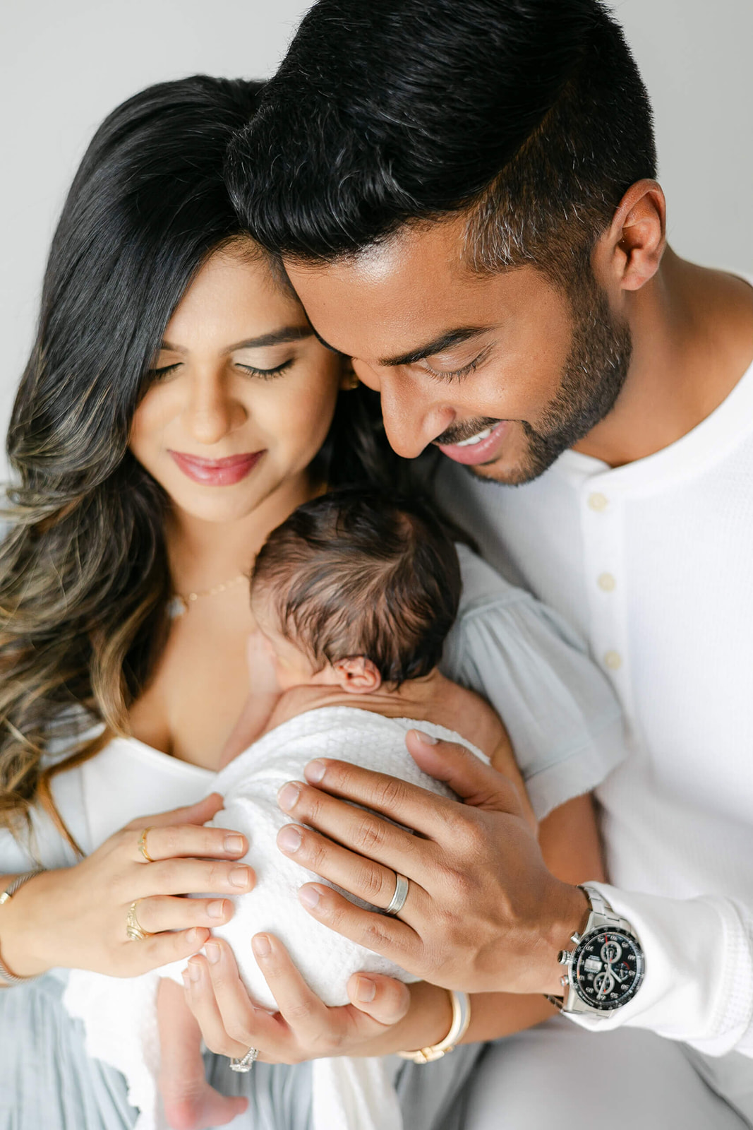 Happy parents cradle their newborn baby against mom's chest while sitting in a studio