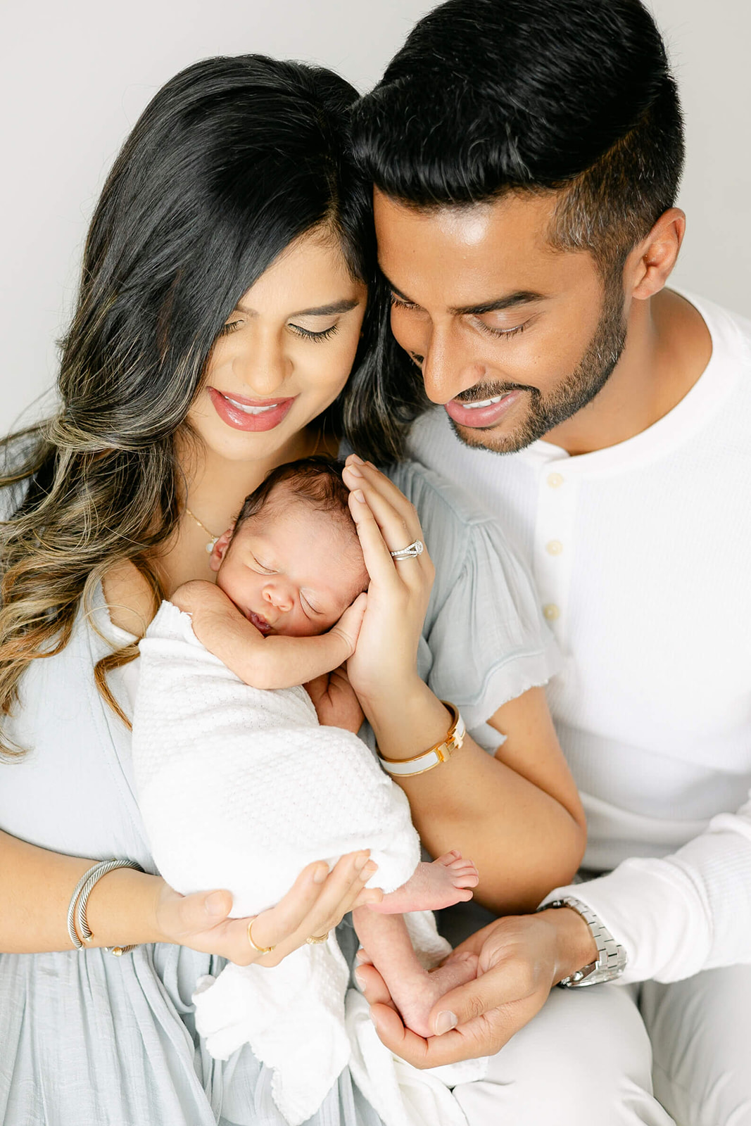 Happy new mom and dad snuggle their sleeping newborn baby against mom's chest while sitting before meeting a Houston Au Pair