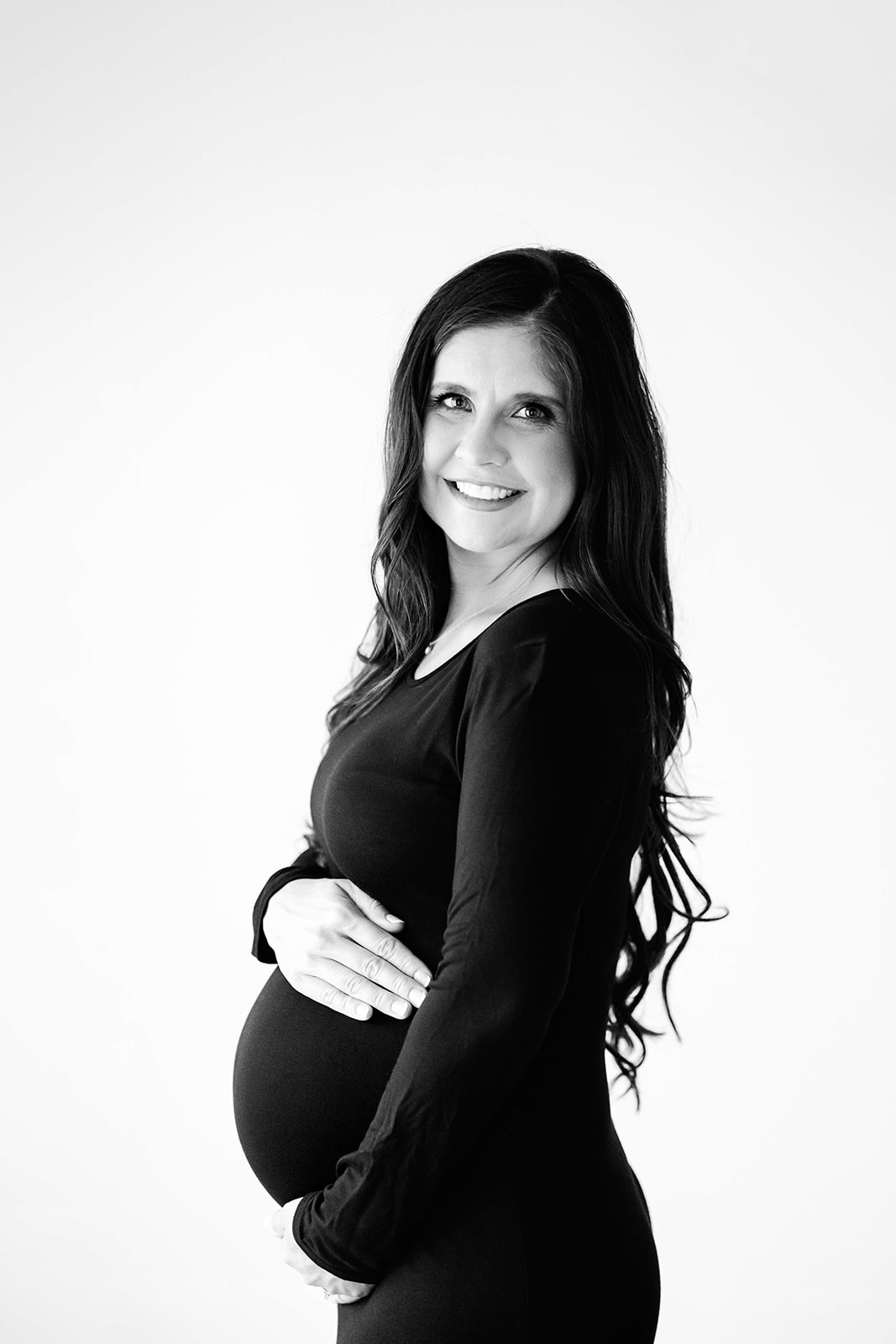 A happy mom to be in a black dress holding her bump in a studio before preparing for Placenta Encapsulation Houston