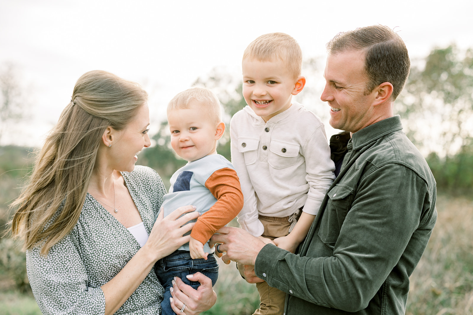 Toddler brothers giggle while playing in mom and dad's arms in a park