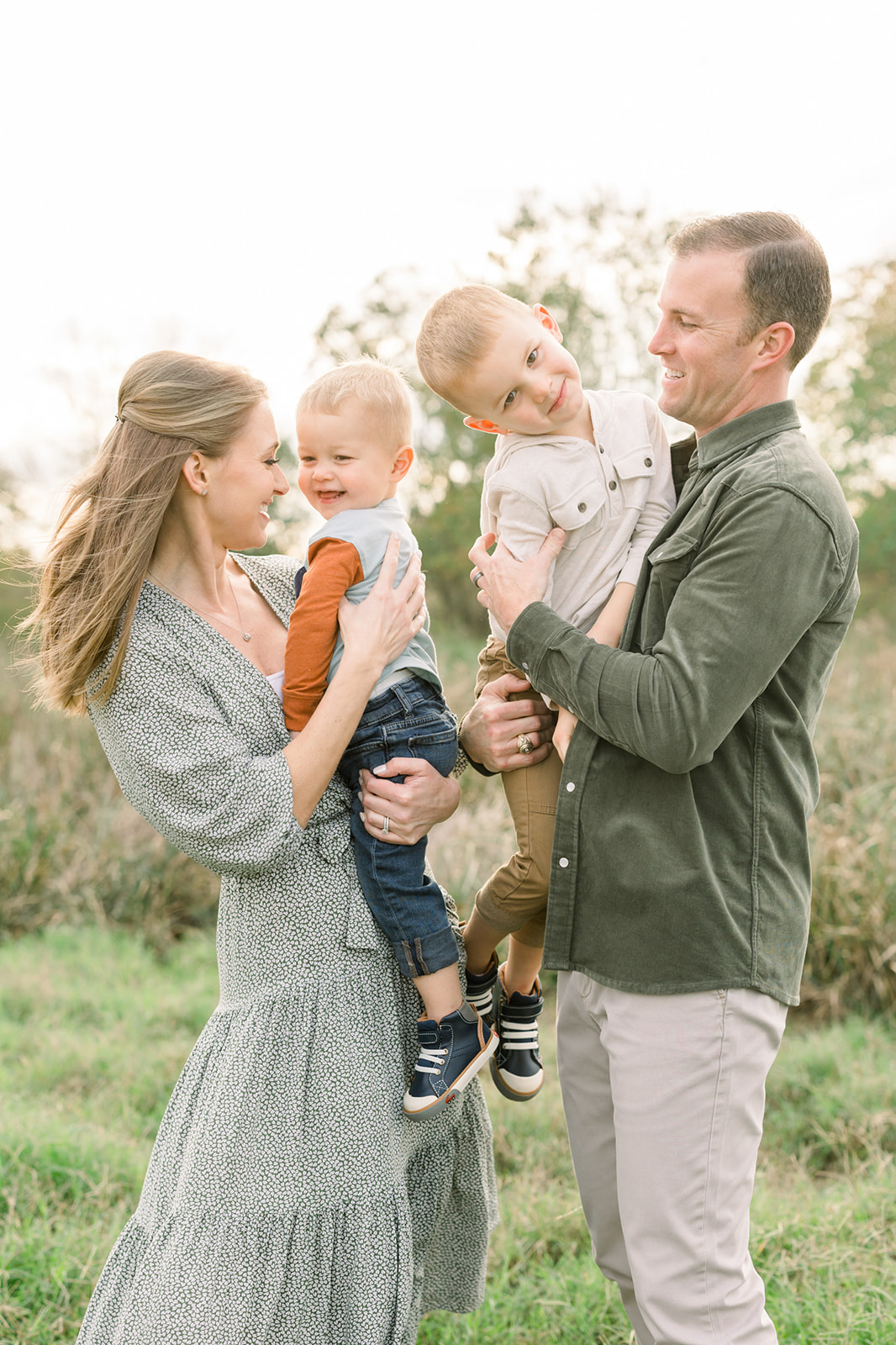 Happy mom and dad stand in a park playing with their toddler sons in their arms before visiting Preschools in Houston